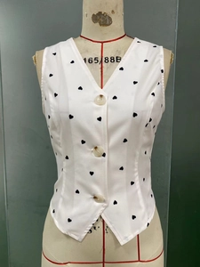 Close-up of white V-neck vest with black heart print and three brown buttons on a mannequin