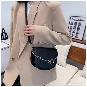 Detail of a black matte saddle bag featuring a gold chain and fashion lettering on a model