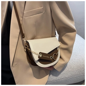 Detail of a two-tone saddle bag with gold chain and fashion tag on beige suit
