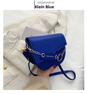 Detail of Klein blue saddle bag with golden chain and fashion leather tag on white fabric
