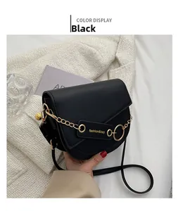 Detail view of black saddle bag with gold ring and chain strap held by a model