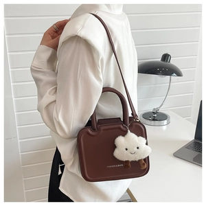 Deep brown leather crossbody bag detail with gold logo and plush cloud charm