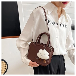 Detail of dark brown crossbody bag with white fluffy cloud charm and fashion slogan