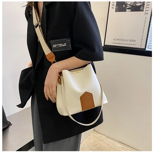 Détail d'un sac seau crème avec patchs en cuir marron et une large bandoulière en toile