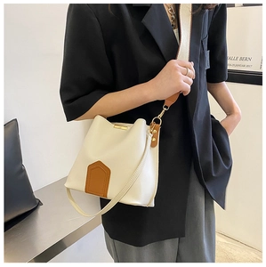 Détail du sac seau minimaliste crème avec écusson marron et bandoulière tissée