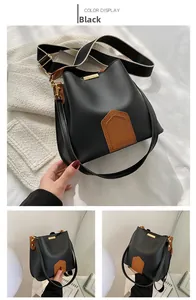Détail du sac seau noir en cuir avec boucles dorées et bandoulière en tissu bicolore