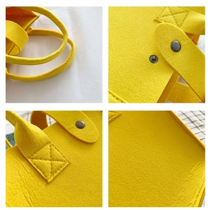 Detail of yellow felt tote bag showing cross-stitching and metal snap button closure