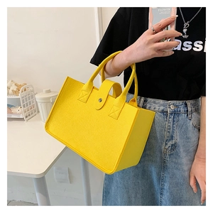 Detail of yellow felt tote bag with button closure and sturdy handle held by a person