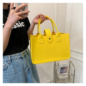 Model holding a vibrant yellow felt tote bag with snap closure in a modern indoor setting