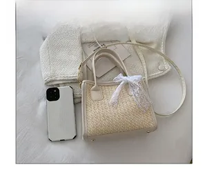 Sac carré en paille avec ruban dentelle et bandoulière à côté d'un téléphone pour la taille