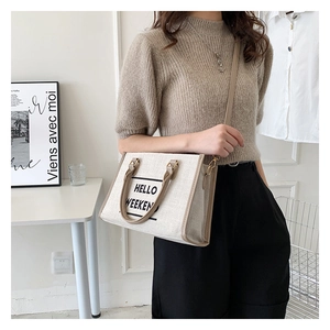 Detail view of canvas tote bag with brown leather trim and HELLO WEEKEND text