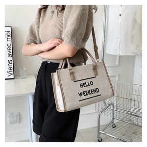Detail of canvas tote bag featuring brown leather handles and Hello Weekend lettering