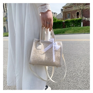 Détail d'un sac à main tissé crème avec nœud en dentelle blanche et clous en métal