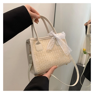 Détail du sac à main en paille tressée avec nœud en dentelle et anses en cuir crème