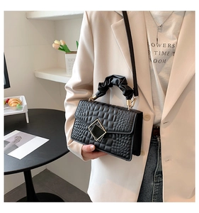 Detail view of black crocodile pattern crossbody bag with ruffled handle and metal buckle