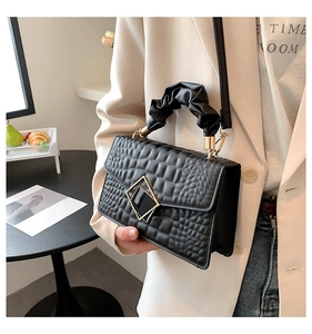 Détail du sac à main noir texture crocodile avec poignée froncée et fermoir géométrique