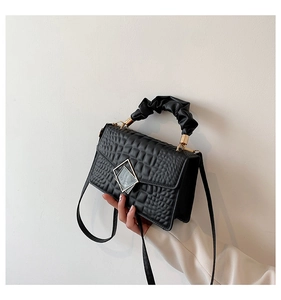 Close-up of black crocodile pattern bag featuring a gold square buckle and ruched handle