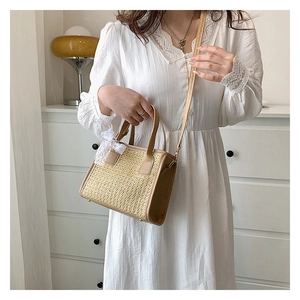 Gros plan du sac bandoulière tressé beige avec nœud en dentelle sur robe blanche