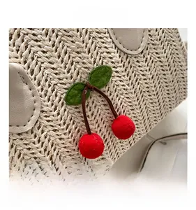 Detail of woven straw bag showing red cherry charms and premium leather trim details