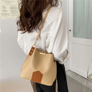 Sac seau beige contrasté avec garniture en cuir marron et boucles dorées porté à l'épaule