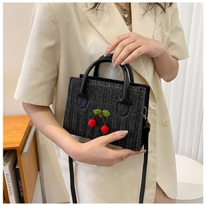Detail of black woven crossbody bag featuring cute cherry decor and refined texture
