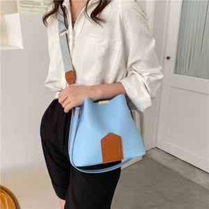 Sac seau bicolore bleu avec garniture en cuir marron porté par un mannequin