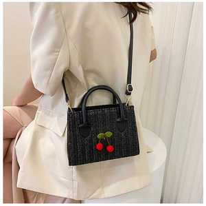 Detail of woven cherry crossbody bag in black with gold hardware on a model