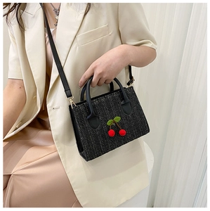 Detail shot of black woven crossbody bag with red cherry accents on a model's hip