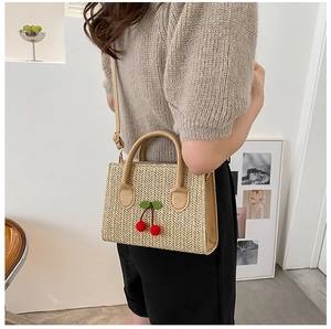 Detail of woven straw crossbody bag with red cherry accents and adjustable leather strap