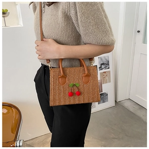 Detail of hand-woven straw crossbody bag with cherry decor on a model's shoulder