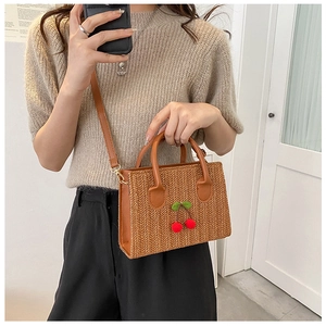 Detail of woven straw handbag featuring 3D red cherry accents and a round handle