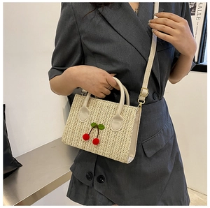 Detail of a woven cherry crossbody bag with red cherry charms and adjustable strap