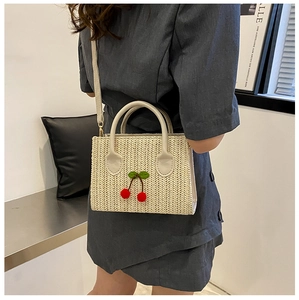 Detail of woven straw crossbody bag with decorative red cherry pom-poms and green leaves