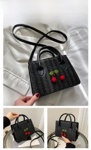 Detailed view of black woven crossbody bag featuring 3D cherry accents and leather straps