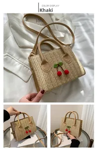 Detail of khaki woven crossbody bag with decorative red cherry charms and leather strap