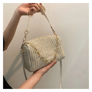 Detail of a beige woven crossbody bag featuring golden chain and circular metal handle