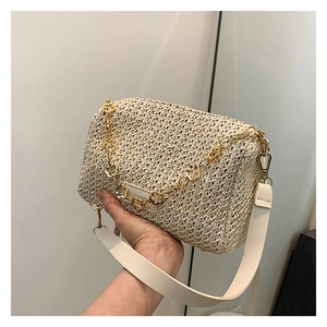 Detail of light beige woven straw bag with gold flower chain and white leather strap