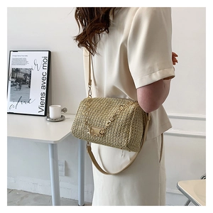 Detail of woven straw crossbody bag featuring metal chain strap and logo plaque