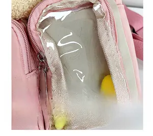 Dettaglio dello zaino rosa con tasca frontale in PVC trasparente e pompon colorati