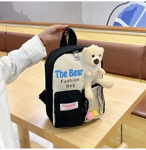 Dettaglio dello zaino bicolore con orsetto di peluche e tasca trasparente con pompon