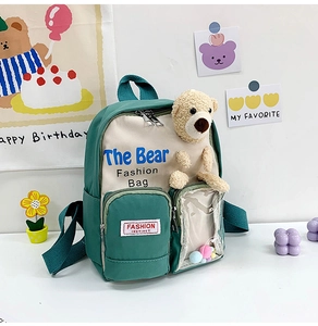 Dettaglio zaino verde per bambini con orsetto di peluche e pompon colorati nella tasca PVC
