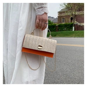 Detail of woven straw and orange leather crossbody bag with gold metal handle and chain