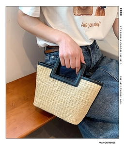 Detail of hand-woven beige straw tote bag with black leather square handles and trim