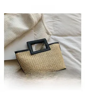 Detail of beige straw weave texture and black leather handle on contrast tote bag