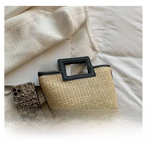 Detail of woven straw tote bag featuring black leather handles and textured weaving