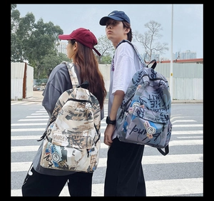 Street style shot of beige and blue graffiti backpacks with logo patches on a city crossing