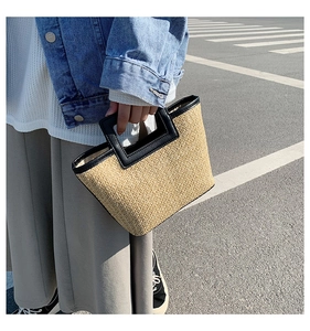Detail of hand-woven straw tote with black leather square handles and stylish trapezoid shape