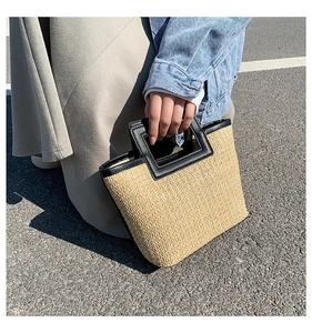 Close-up of woven straw tote bag with black faux leather handles and modern texture