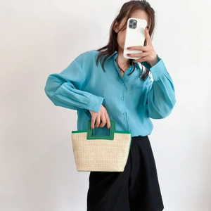 Close-up of woven straw tote bag with green handles paired with a blue shirt and black shorts