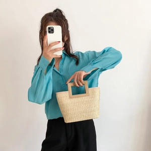 Detail of a beige woven straw tote bag with rectangular handles and vacation style